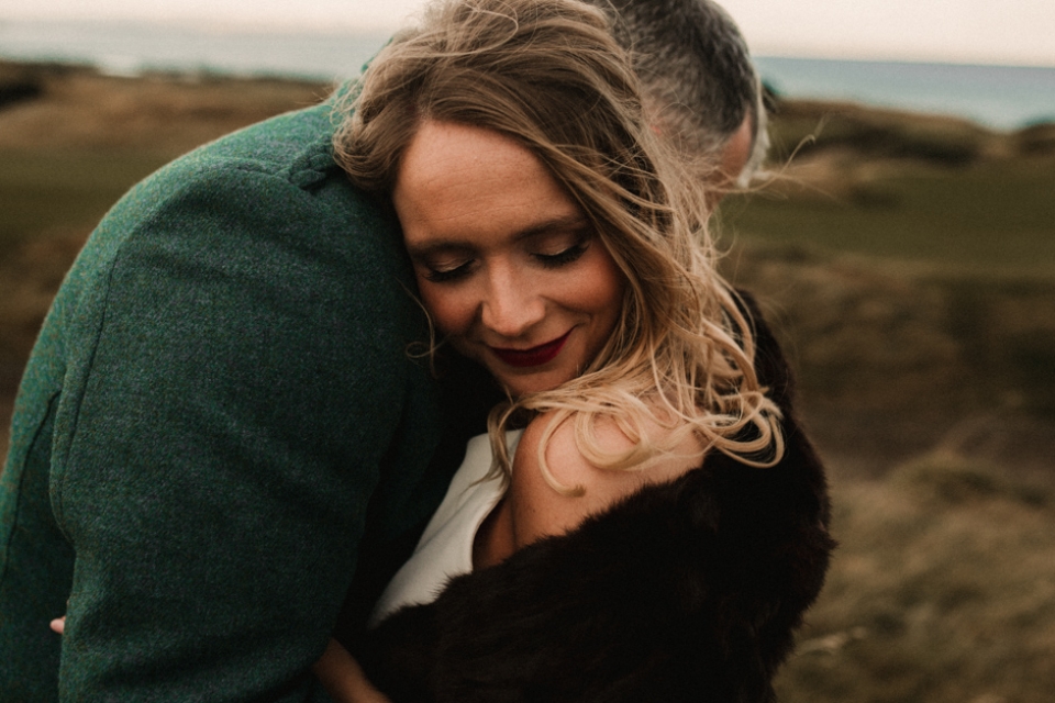 bride and groom keeping warm on the sand dunes , natural wedding photography