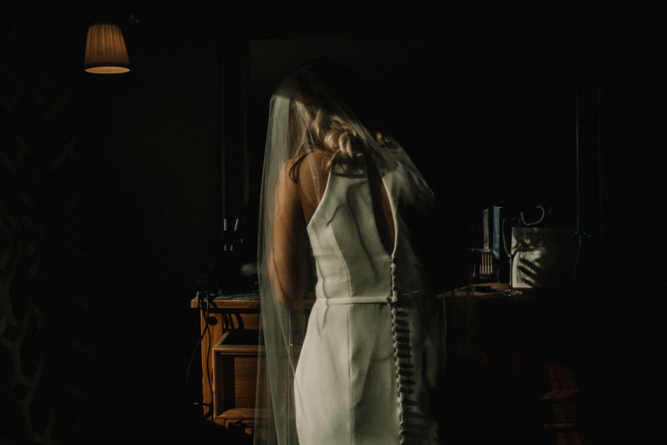 bride putting her lipstick on in the mirror , light catching her veil