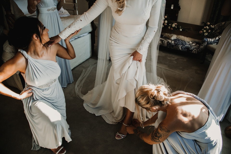 bridesmaids helping bide into her shoes