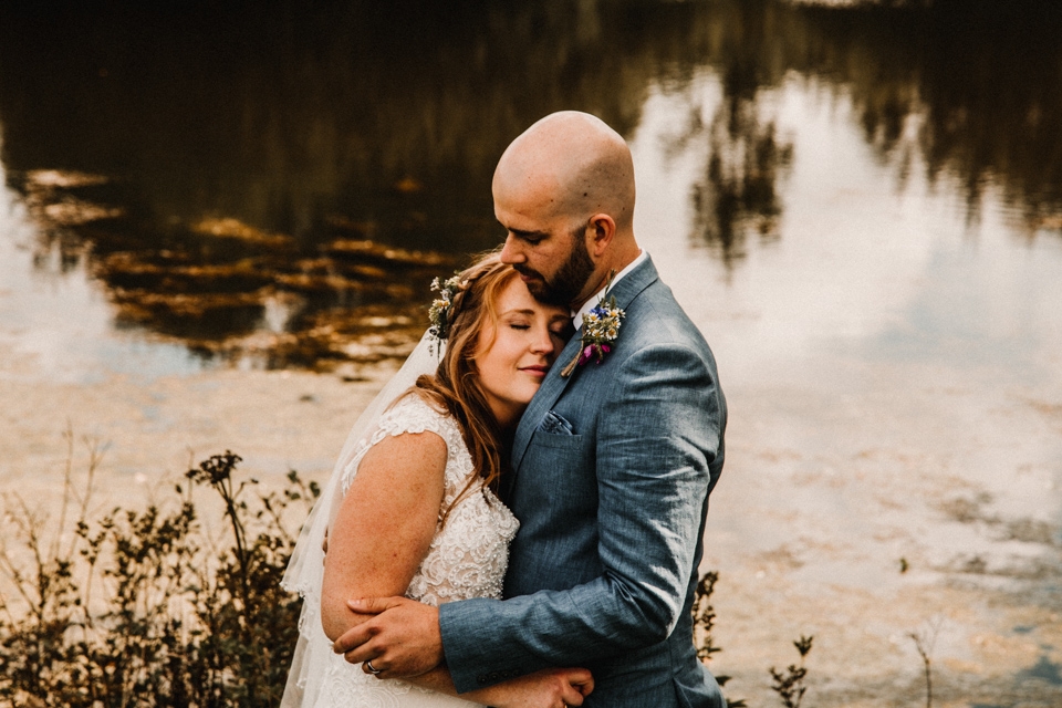 couple cuddles bride and groom at buckland house boating lake