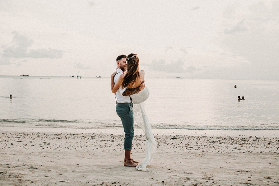 bride and lifts his wife up and plays by spinning her around on the beach