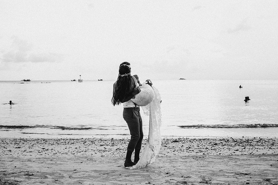 black and white image of groom lifting his wife up on the beach.