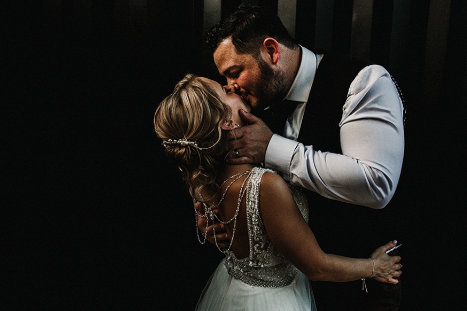 Bride and groom having a passionate cuddle next to a black farm tank