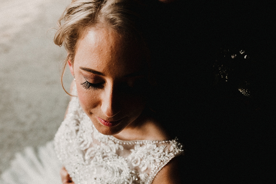 light falling on brides face and groom can be faintly seen kissing her
